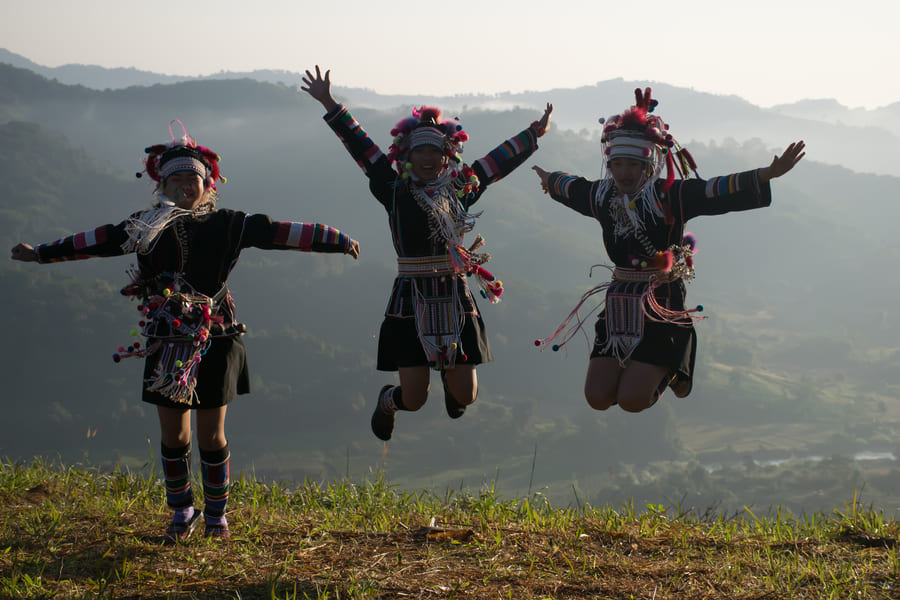 Tres mujeres de la etnia Akha saltando de alegría con trajes tradicionales en una colina de China. Vive experiencias culturales auténticas y encuentros locales únicos con Destino China.
