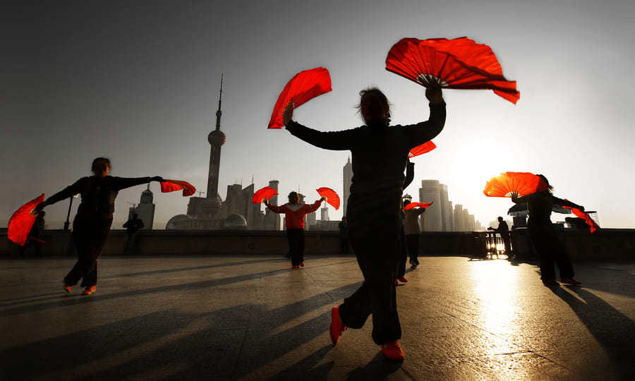 Personas practicando la danza tradicional con abanicos rojos en el Bund de Shanghái al amanecer. Vive la cultura local del día a día con los viajes personalizados a China de Destino China.