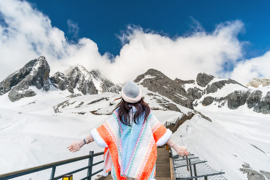 Viajera contemplando la majestuosa Montaña de Nieve del Dragón de Jade en Yunnan. Explora la naturaleza profunda con nuestra agencia de viajes a China a la medida.