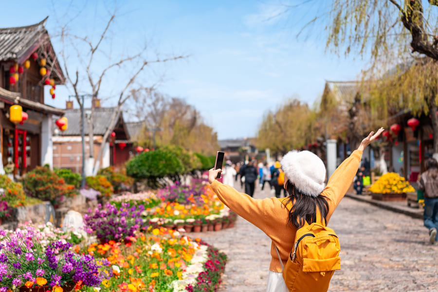 Viajera con mochila amarilla celebrando con los brazos abiertos en una calle histórica de Yunnan. Diseña tu aventura ideal con nuestra agencia de viajes a China a la medida.